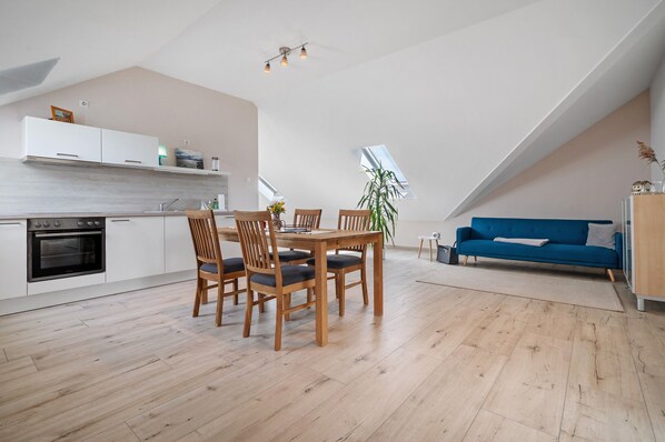Eine moderne Küche mit weißen Schränken, einem Esstisch mit Stühlen und einem blauen Sofa in einem Wohnbereich im Loft-Stil.