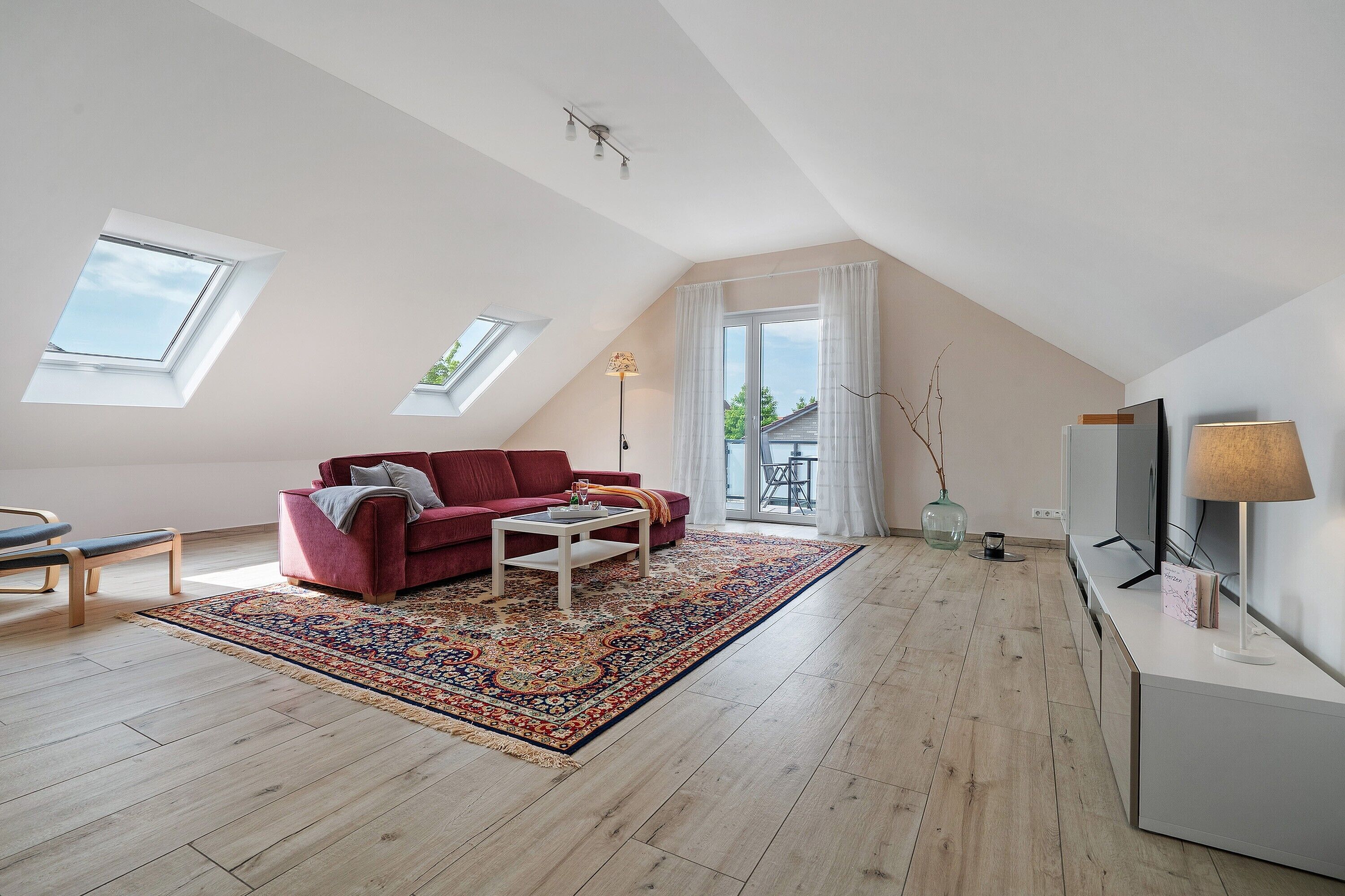 Un appartement moderne de style « loft » avec un canapé rouge, une table basse, un téléviseur et une grande fenêtre.