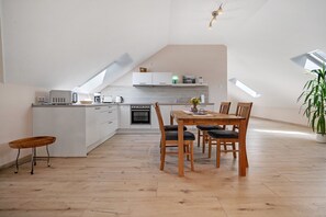Eine moderne Küche mit weißen Schränken, ein Essbereich mit Holztisch und -stühlen sowie ein Oberlicht.