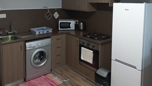 Eine kompakte Küche mit Holzausstattung, einer Mikrowelle, einem Gasherd, einer Waschmaschine und einem Kühlschrank.