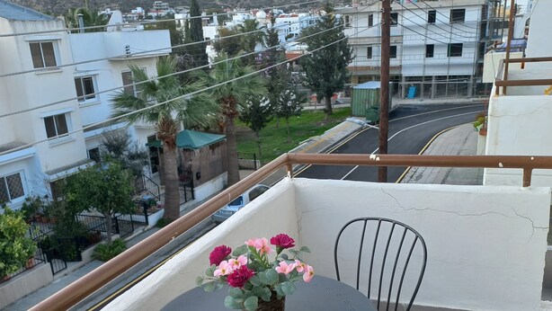 Ein Balkon mit rundem Tisch und zwei Stühlen, mit Blick auf ein Wohngebiet mit Gebäuden und einer Straße.