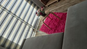 Ein modernes Wohnzimmer mit einem grauen Sofa, einem flauschigen pinkfarbenen Teppich und einer Holz-TV-Konsole.