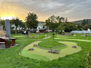 Ein Minigolfplatz mit einer Holzbank, einem kleinen Gebäude und einer Flagge.