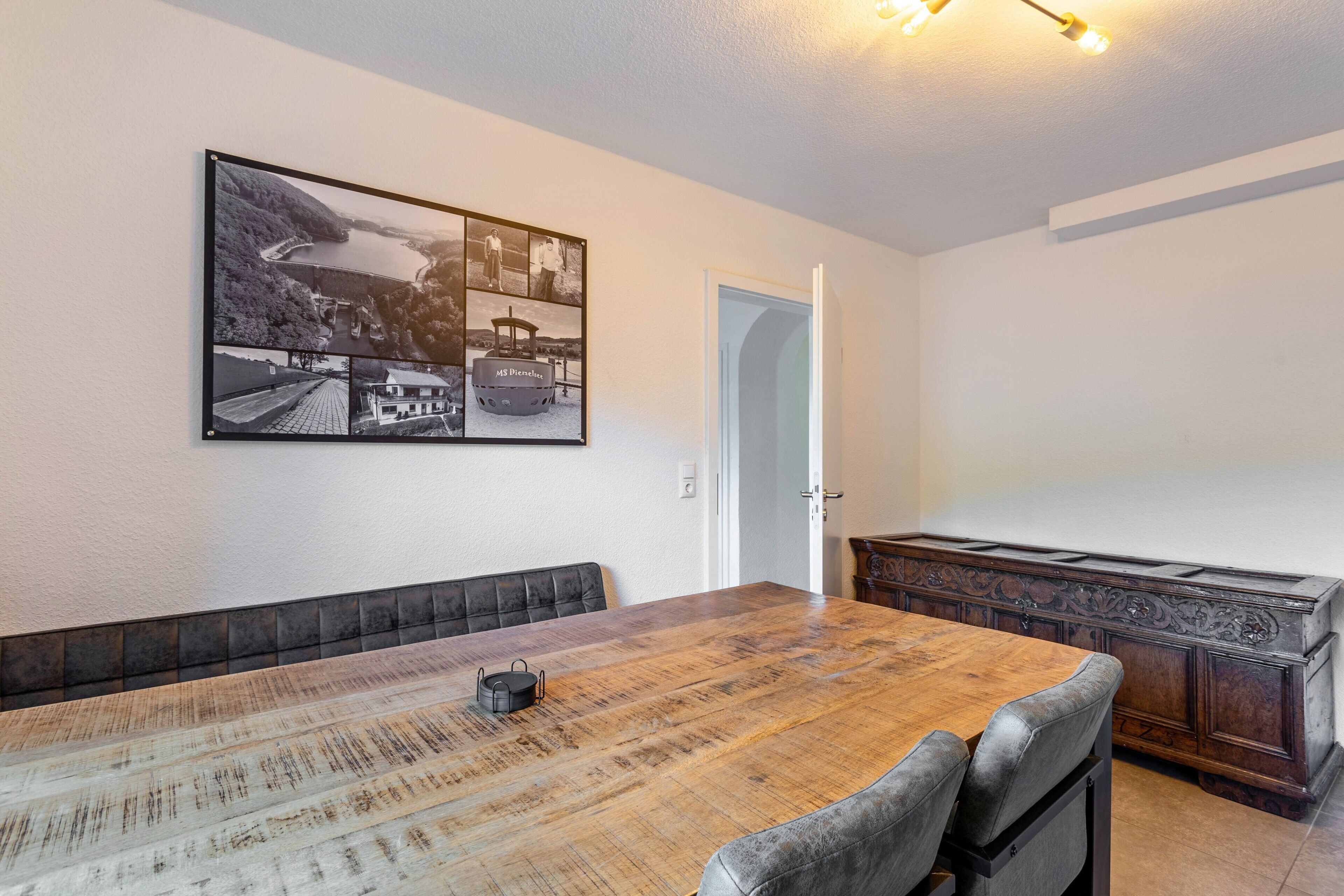 A dining area with a wooden table, cushioned bench seating, a dark wooden cabinet, and a wall-mounted photograph.