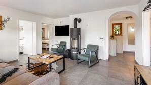 Een moderne woonkamer met een open haard, zitmeubels, een televisie en een keuken die zichtbaar is door een boog.