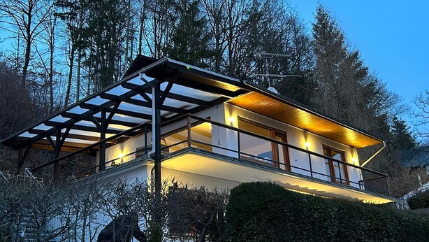 Een modern huis met twee verdiepingen en een balkon, omringd door bomen.