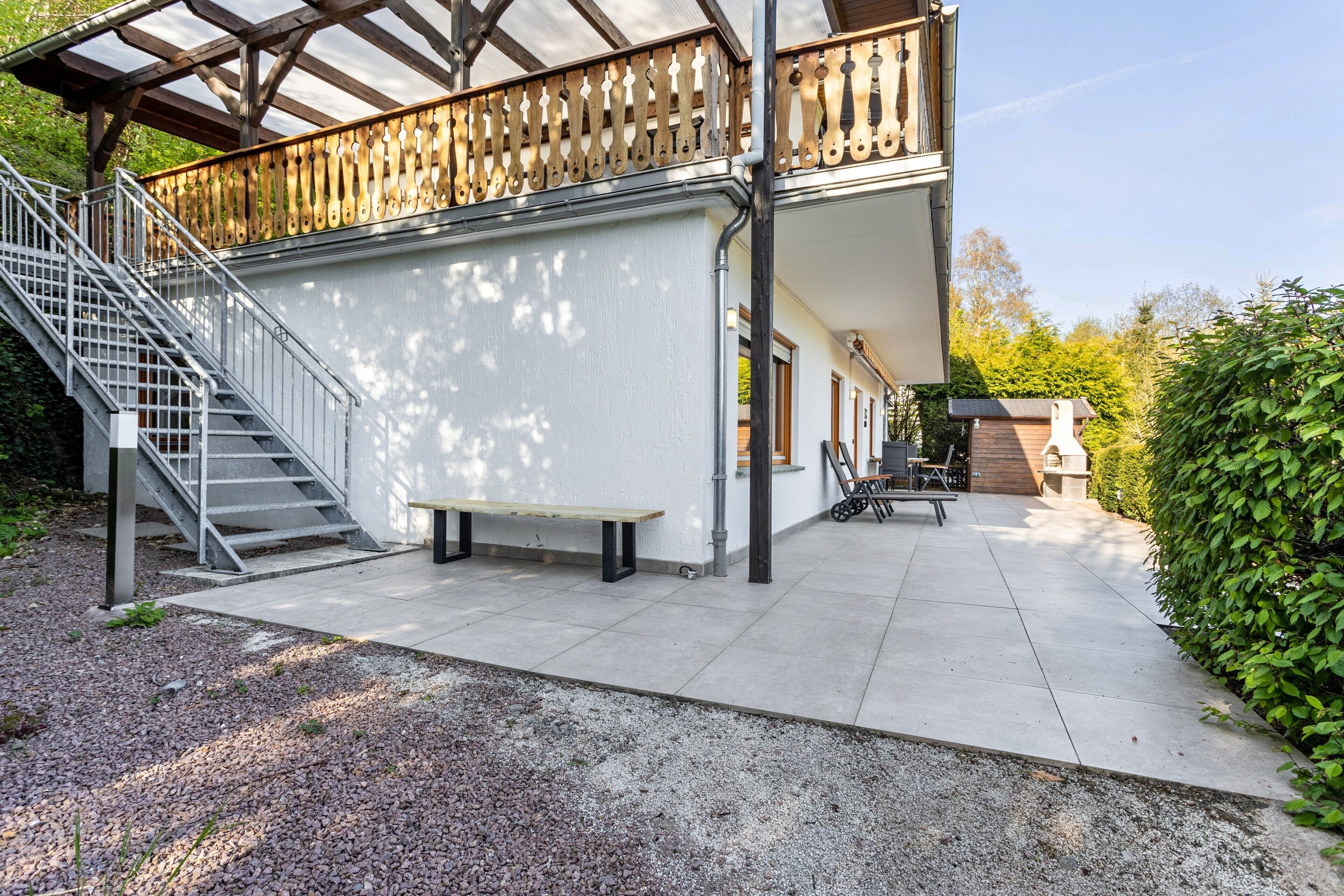 Ein überdachter Außenbereich mit Holzzaun, Metalltreppe und einer Bank.