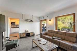 Ein modernes Wohnzimmer mit Sofa, Couchtisch und Blick auf einen Wald durch ein großes Fenster.