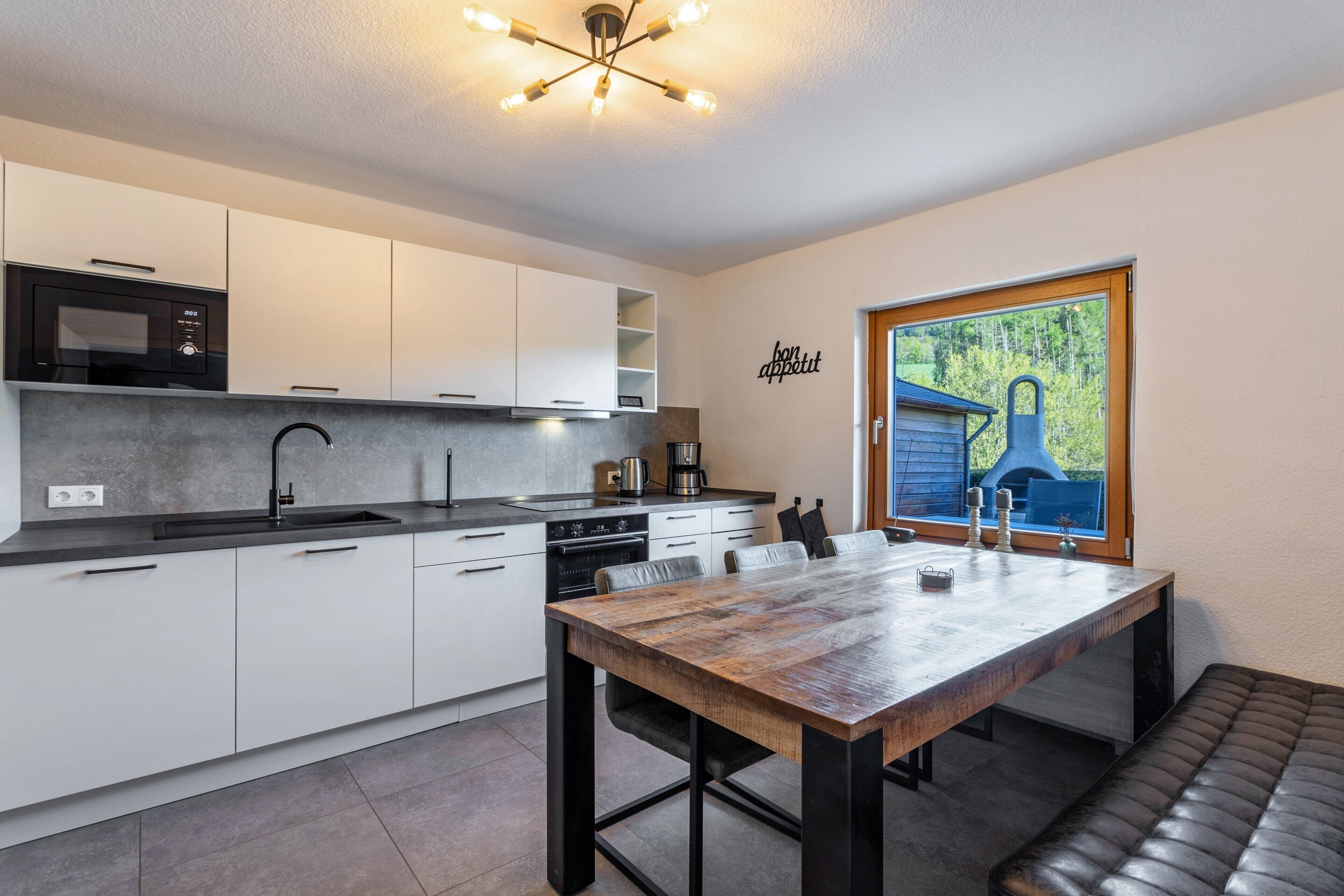 A modern kitchen with white cabinets, a black microwave, and a wooden dining table with a bench.