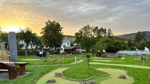 A miniature golf course with a wooden bench, a small building, and a flag.
