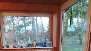 Un intérieur en bois avec un banc rembourré, une fenêtre donnant sur les arbres et un oiseau à l’extérieur.