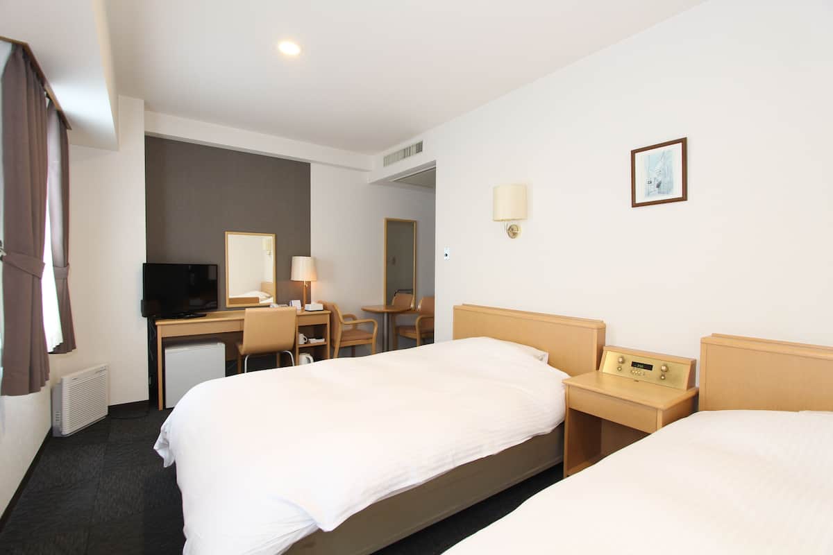 A hotel room with two beds, a desk with a chair, a television, a lamp, and a bedside table with a clock.