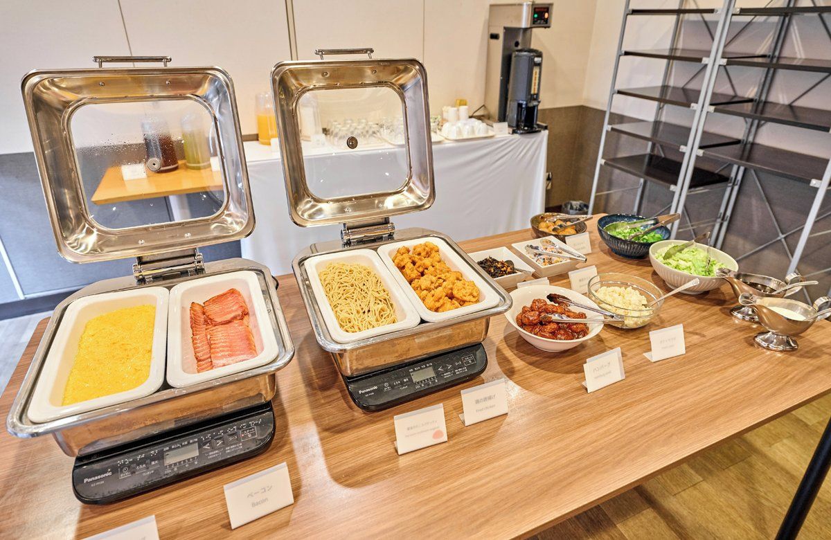 A buffet setup with various food items and a Panasonic rice cooker.