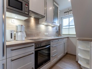 A modern kitchen with stainless steel appliances, a built-in oven, and a window providing natural light. - Ferienwohnung in St. Peter-ording (St. Peter-Ording)