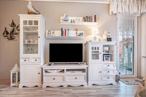 Ein Wohnzimmer mit Fernseher, weißen Schränken, Bücherregalen und Dekorationselementen.