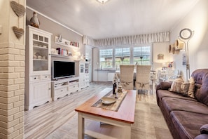 A living room with a television, white cabinets, a brown leather couch, and a dining area with a table and chairs.