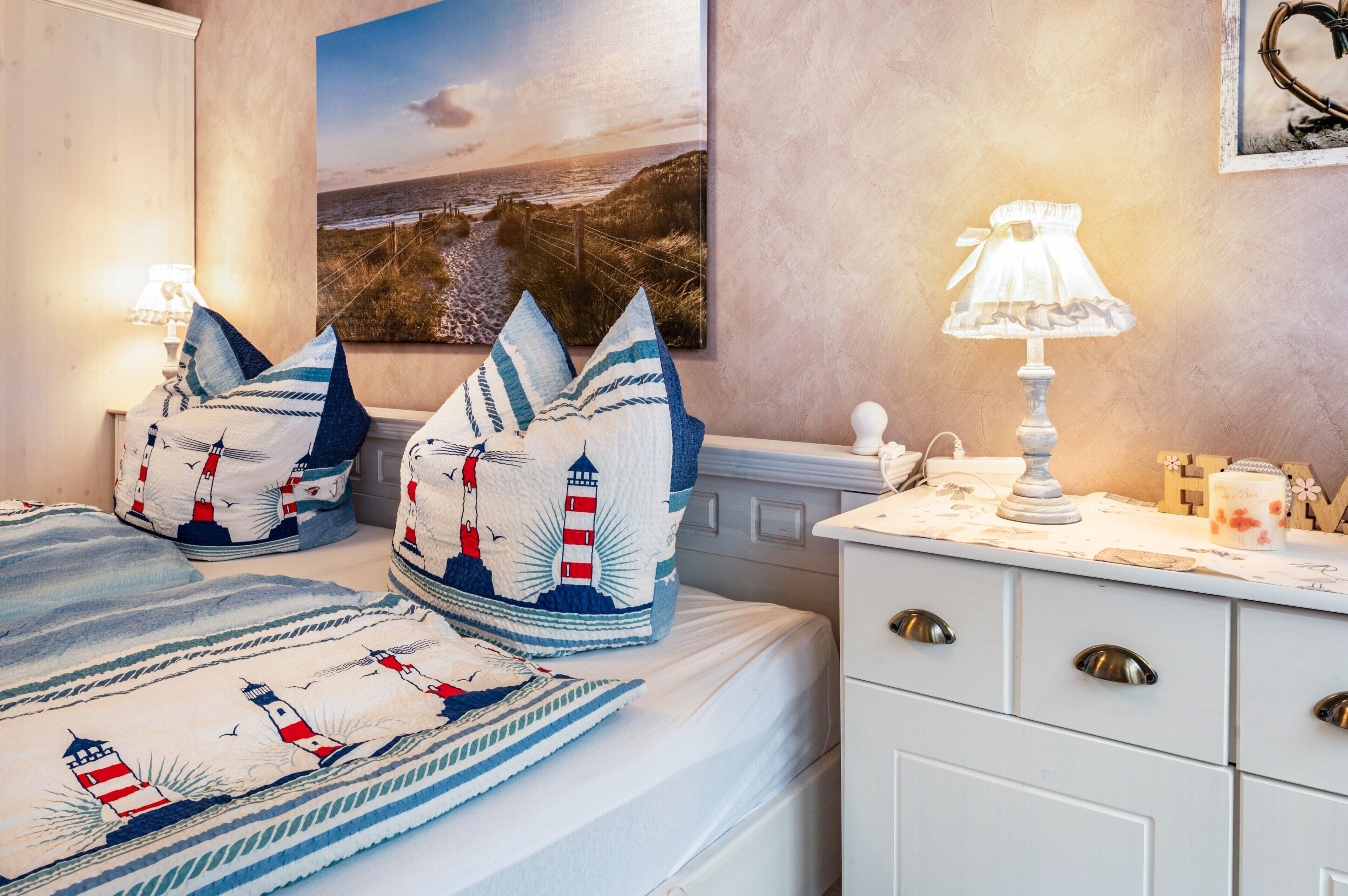 Un lit bien fait, avec une couverture à rayures et des oreillers, une table de chevet avec une lampe, et un tableau accroché au mur.