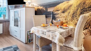 Ein Zimmer mit Esstisch für zwei Personen, einem Fernseher auf einem Schrank und einem Fenster mit Vorhängen.