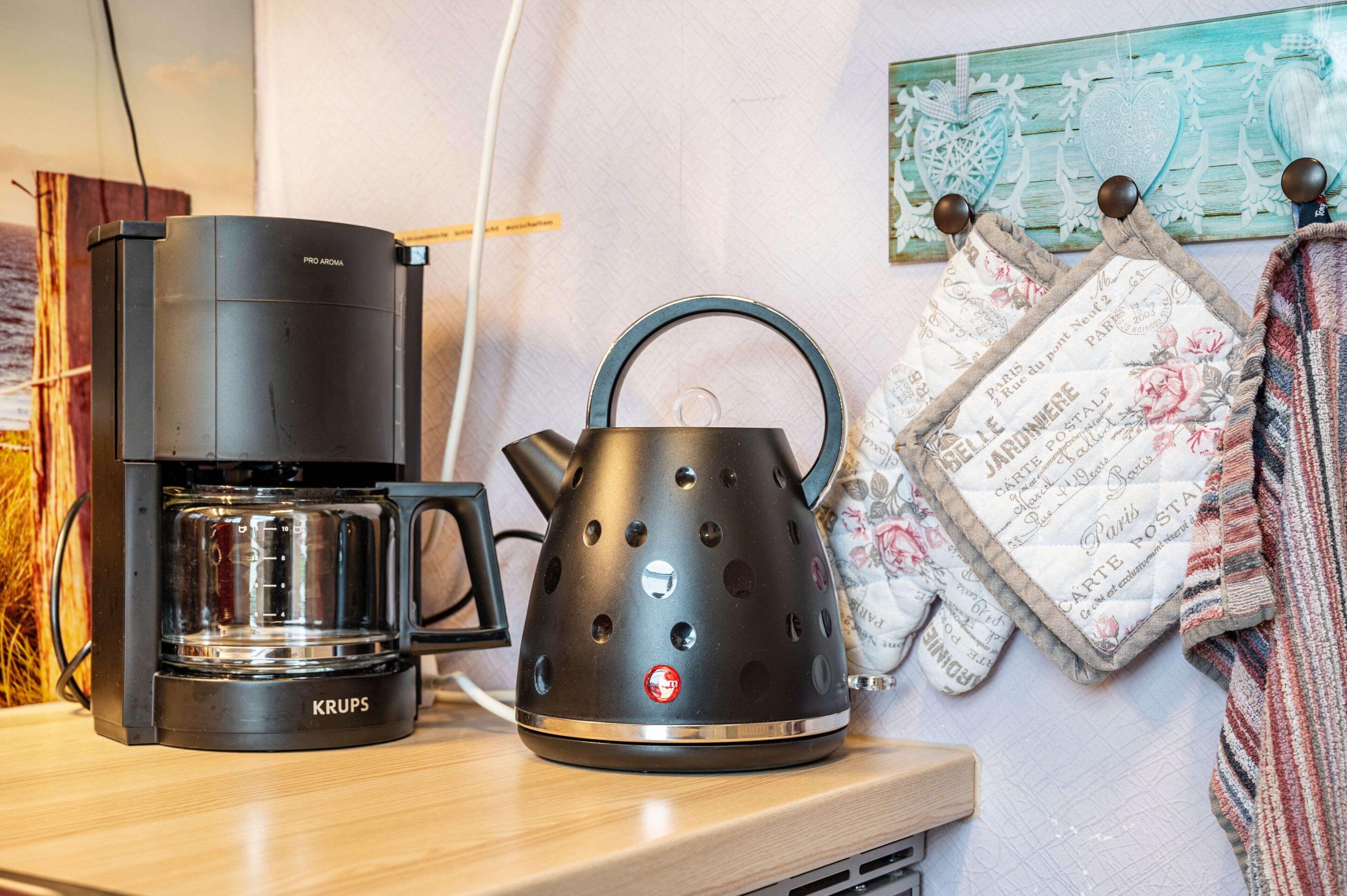 A coffee maker and kettle on a wooden surface, with a wall-mounted towel rack and a decorative item in the background.