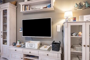 Et værelse med et fladskærms-tv, en reol, et skab med service og en lampe.
