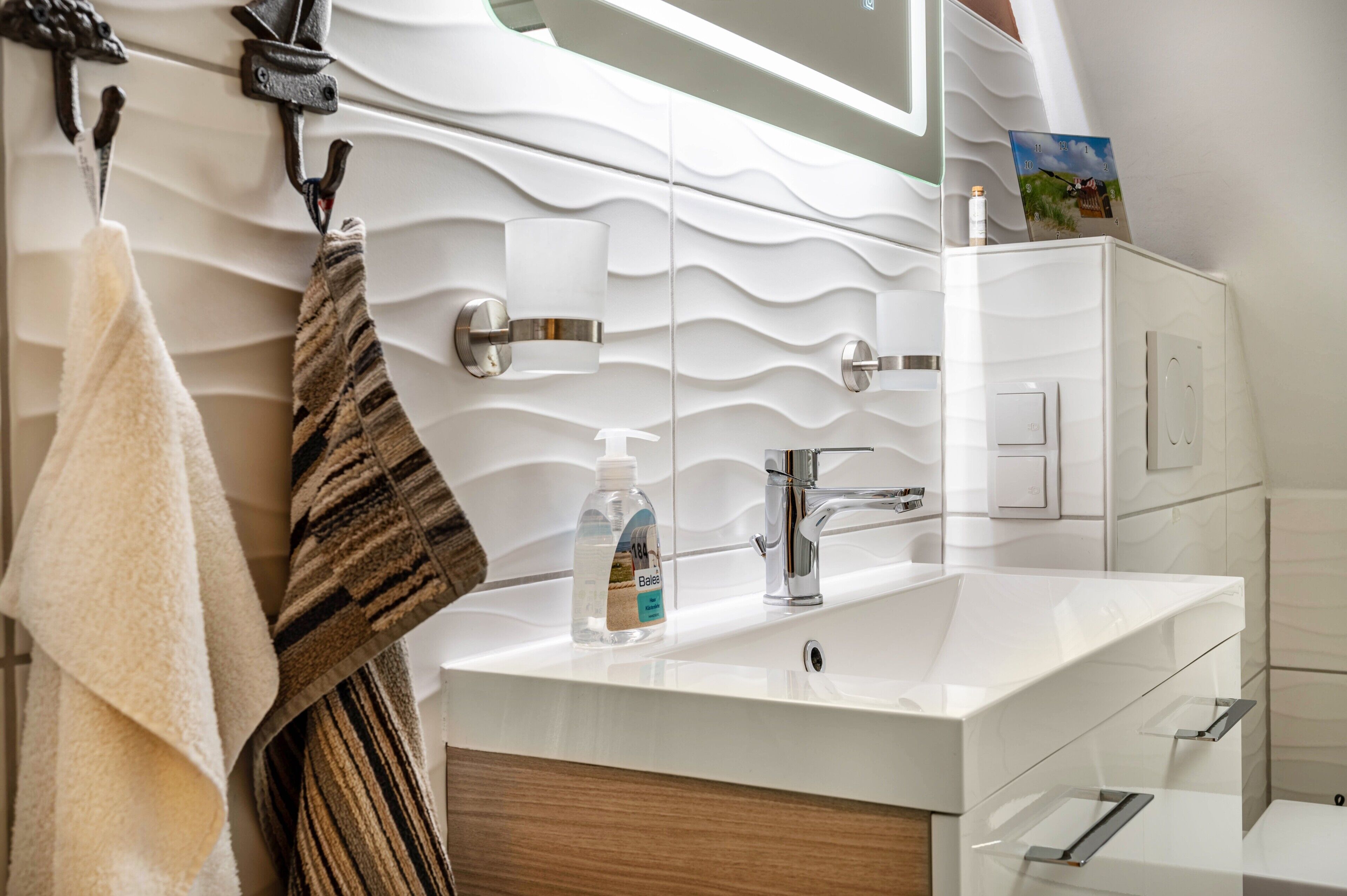 A modern bathroom with a white sink, a towel rack with a towel, a soap dispenser, and a mirror.