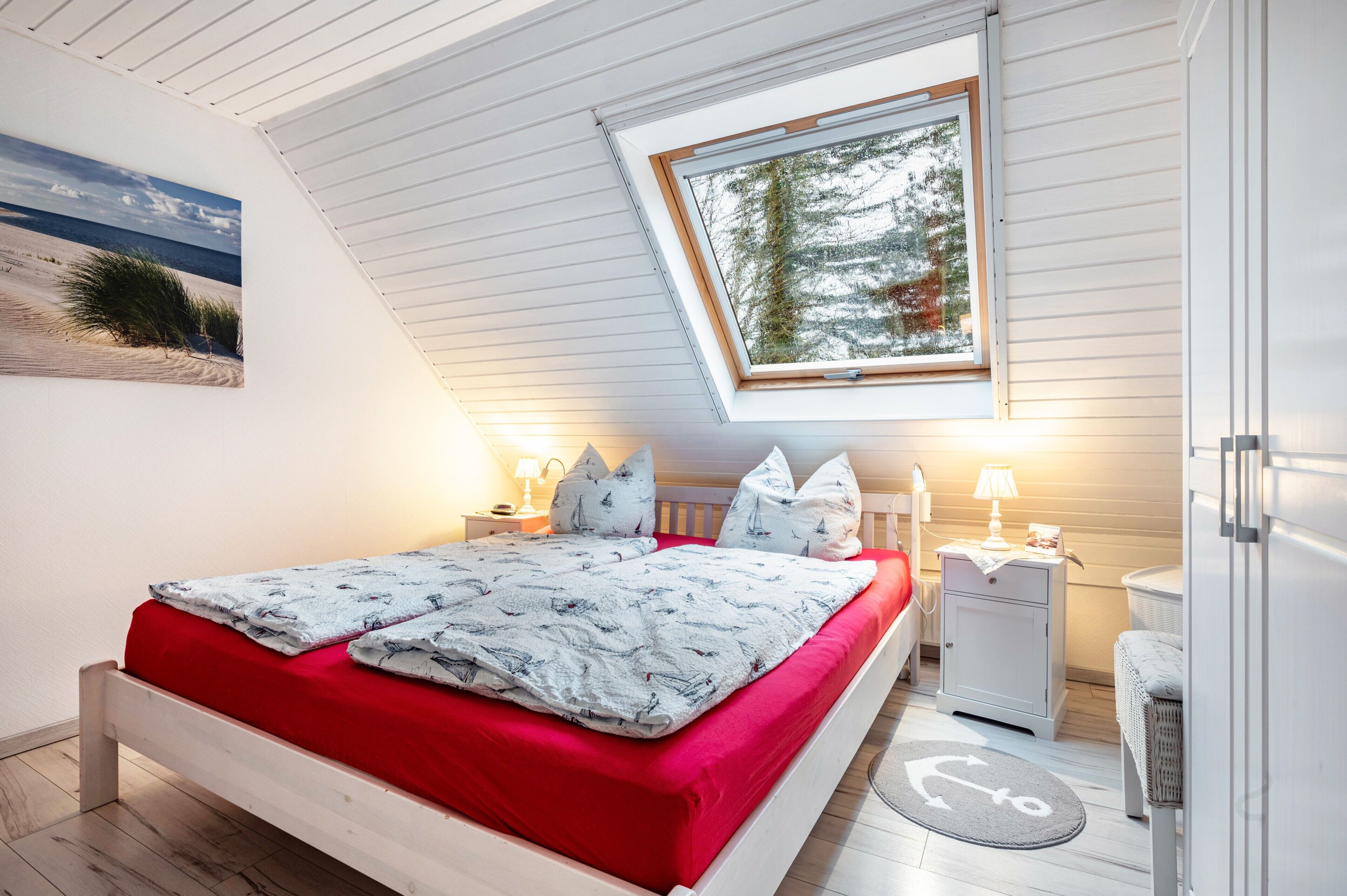 A bedroom with a bed, a nightstand, a lamp, a window with a view of trees, and a painting on the wall.