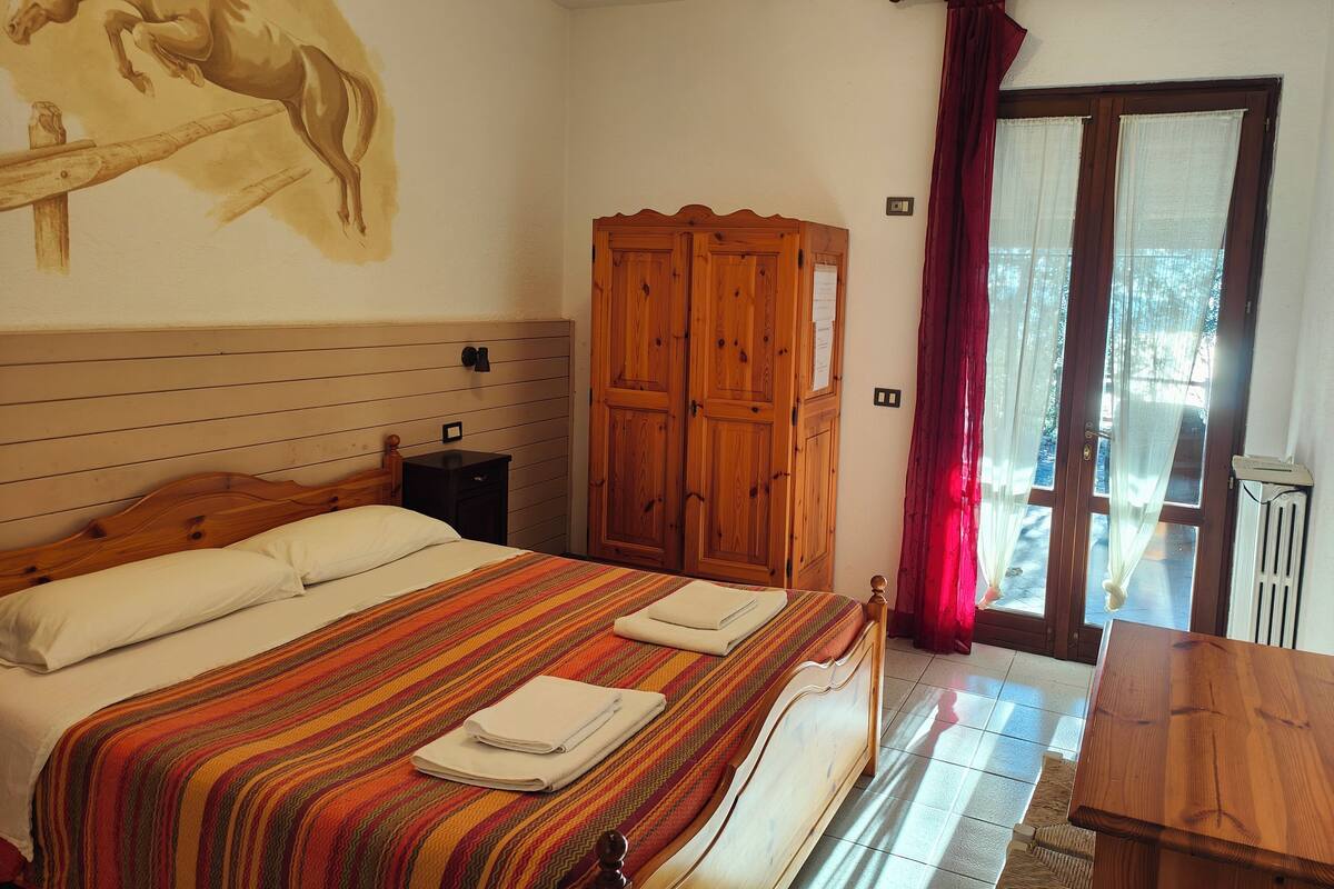A bedroom with a wooden bed, a wooden wardrobe, a small bedside table, and a window with curtains.