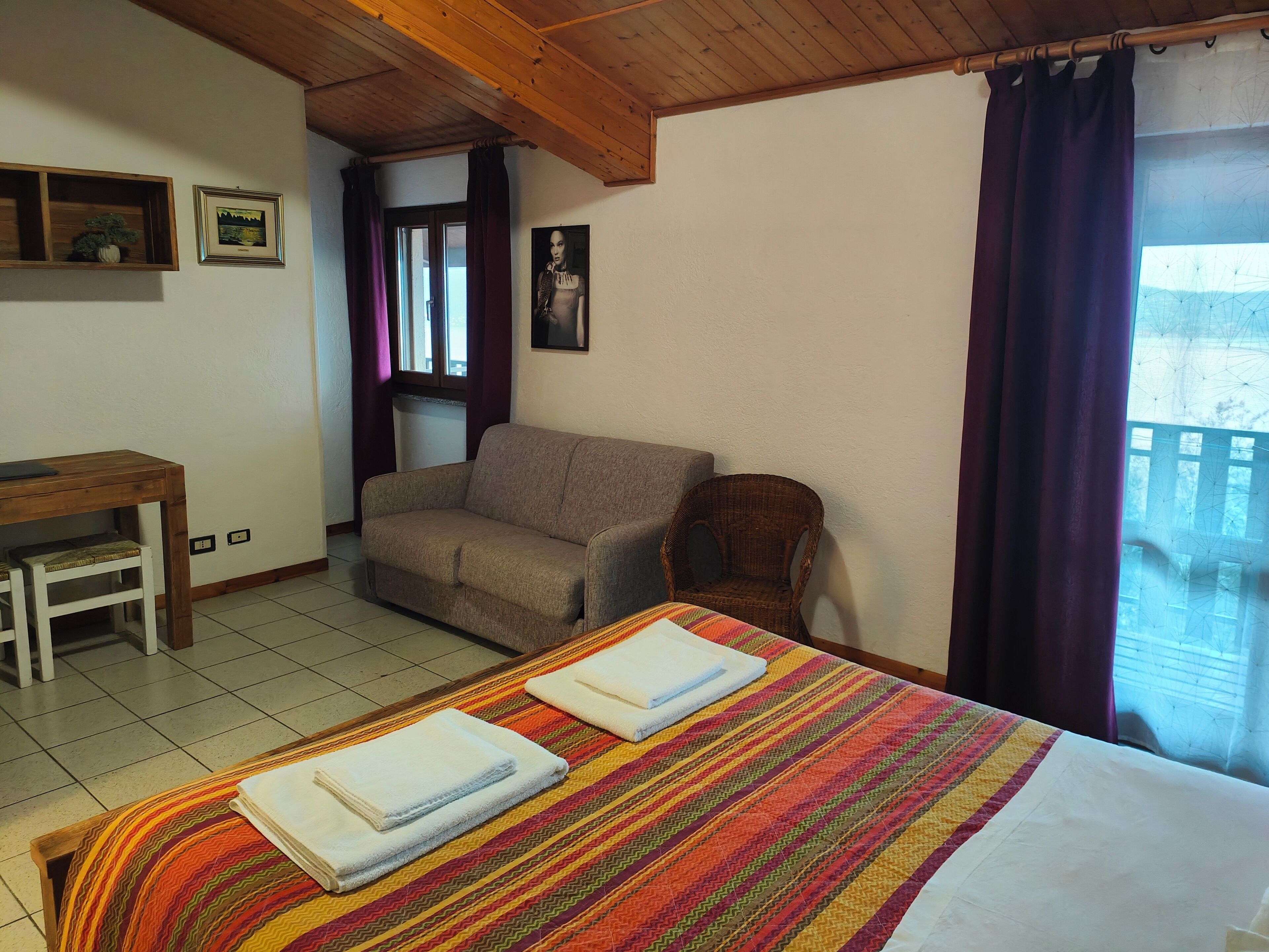Un dormitorio con cama, sofá, sillón, una mesita y una ventana con cortinas.