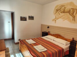 Une chambre à coucher avec un lit en bois, deux tables de chevet, une armoire en bois, une porte et deux tableaux encadrés accrochés au mur.