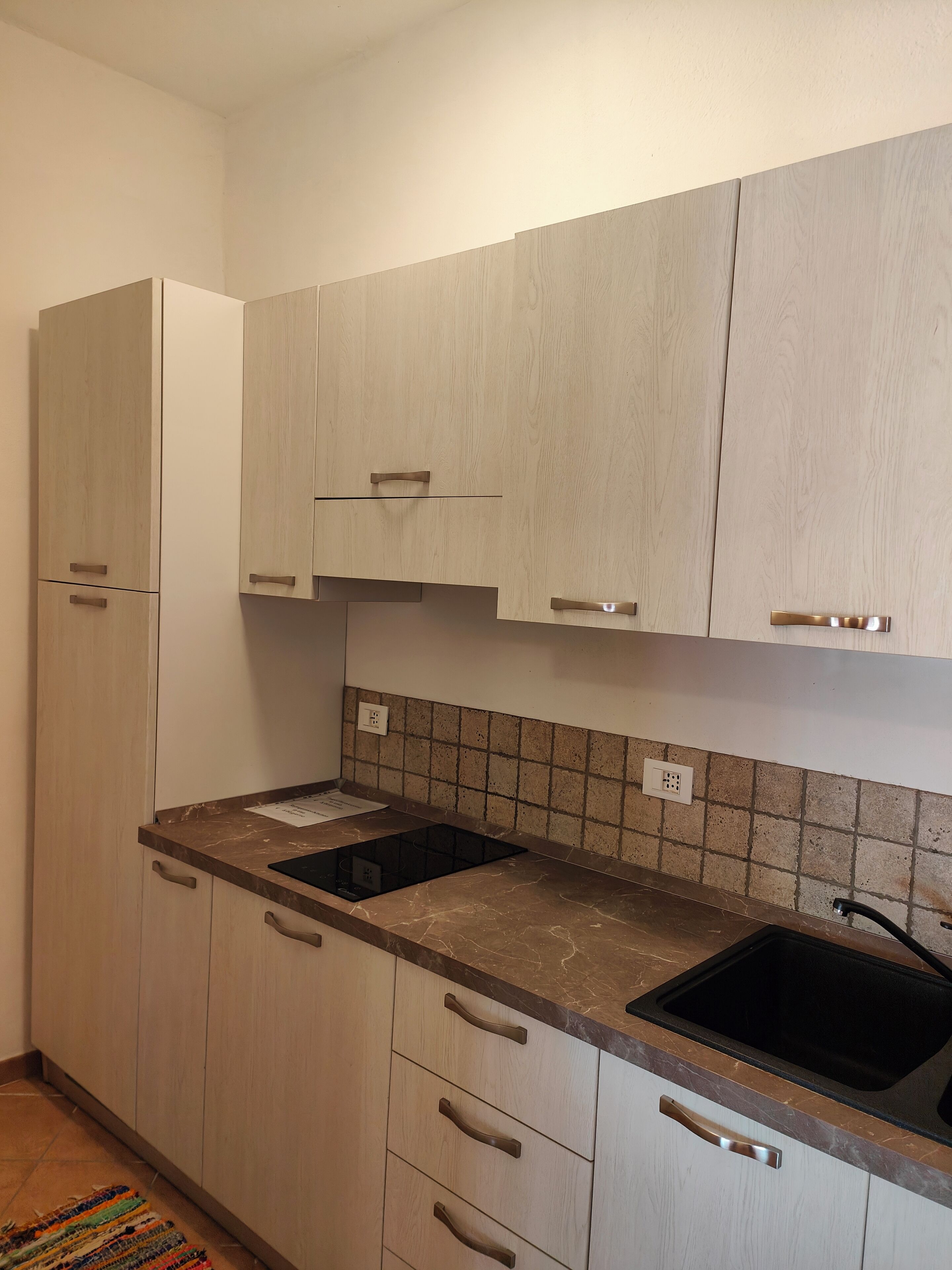 A kitchen with light wood cabinets, a marble countertop, and a black sink.