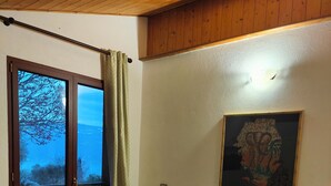 A bedroom with a bed, a window with a view, a painting on the wall, and a wooden ceiling. - Agriturismo Scuderia Castello (Toscolano Maderno)