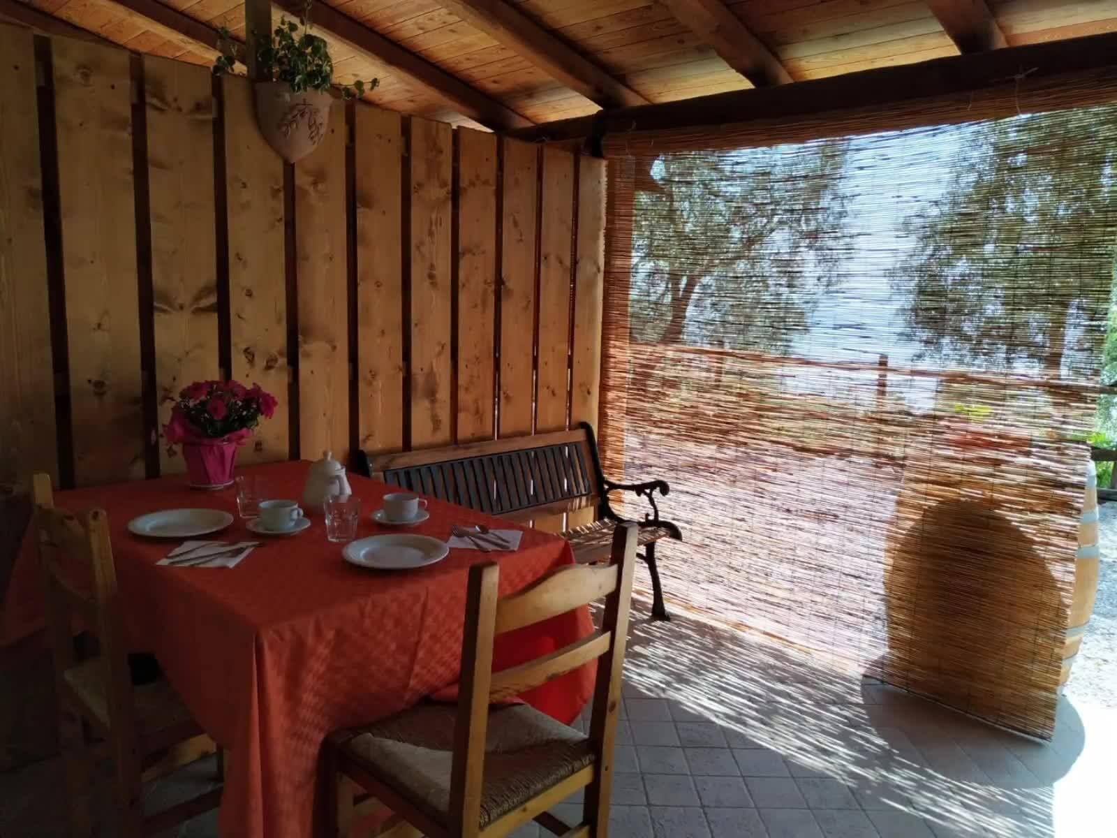 A wooden dining area with a table set for two, a bench, and a hanging plant.