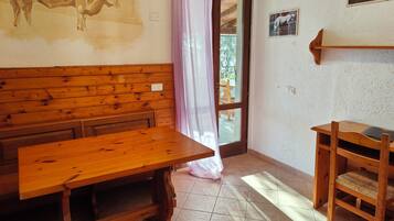 Un banco y una mesa de madera en una habitación de estilo rústico, una puerta que da al exterior y un pequeño estante de madera.