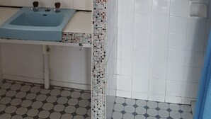 A bathroom with a blue sink, a mirror, a shower with a metal rod, and tiled walls with a decorative border. - Hillocks Homestead Overlooking the Bush (Marion Bay)