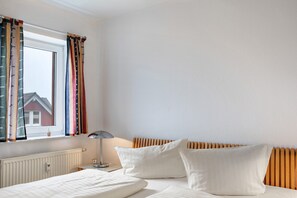 A bedroom with a bed, a window with curtains, a radiator, and a lamp. - Apartment 'Tannenblick 2-4' with Mountain View, Balcony and Wi-Fi (Oberhof)