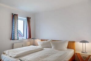 Un dormitorio con cama, dos mesitas de noche, una ventana con cortinas y un radiador.
