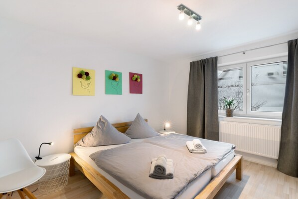 Ein Schlafzimmer mit einem Bett, Nachttischen, einer Lampe und einem Fenster mit Vorhängen.