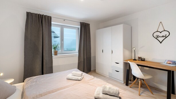 A bedroom with a bed, a desk, a chair, a wardrobe, and a window with curtains. - Apartment 'Hildas Plätzchen' with Private Terrace and Wi-Fi (Oberkirch)