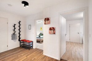 A hallway with a coat rack, a bench with red cushions, and artwork on the walls.