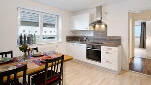 A modern kitchen with white cabinetry, a built-in oven, and a dining area with a wooden table and chairs. - Apartment 'Hildas Plätzchen' with Private Terrace and Wi-Fi (Oberkirch)