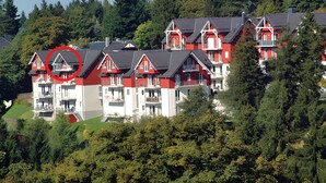 A residential building with multiple balconies, red and white exterior, and surrounded by dense greenery.