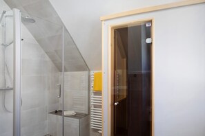 A modern bathroom with a glass shower enclosure, a white radiator, and a wooden door.
