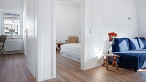 A modern room with a bed, a blue sofa, a small table, and a window with blinds. - Apartment 'Die Alter Schwede 2' with Shared Terrace and Wi-Fi (Vechta)