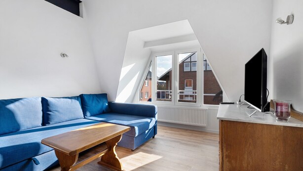 A modern living room with a blue sofa, wooden coffee table, and a TV on a white cabinet. - Apartment 'Die Alter Schwede 2' with Shared Terrace and Wi-Fi (Vechta)