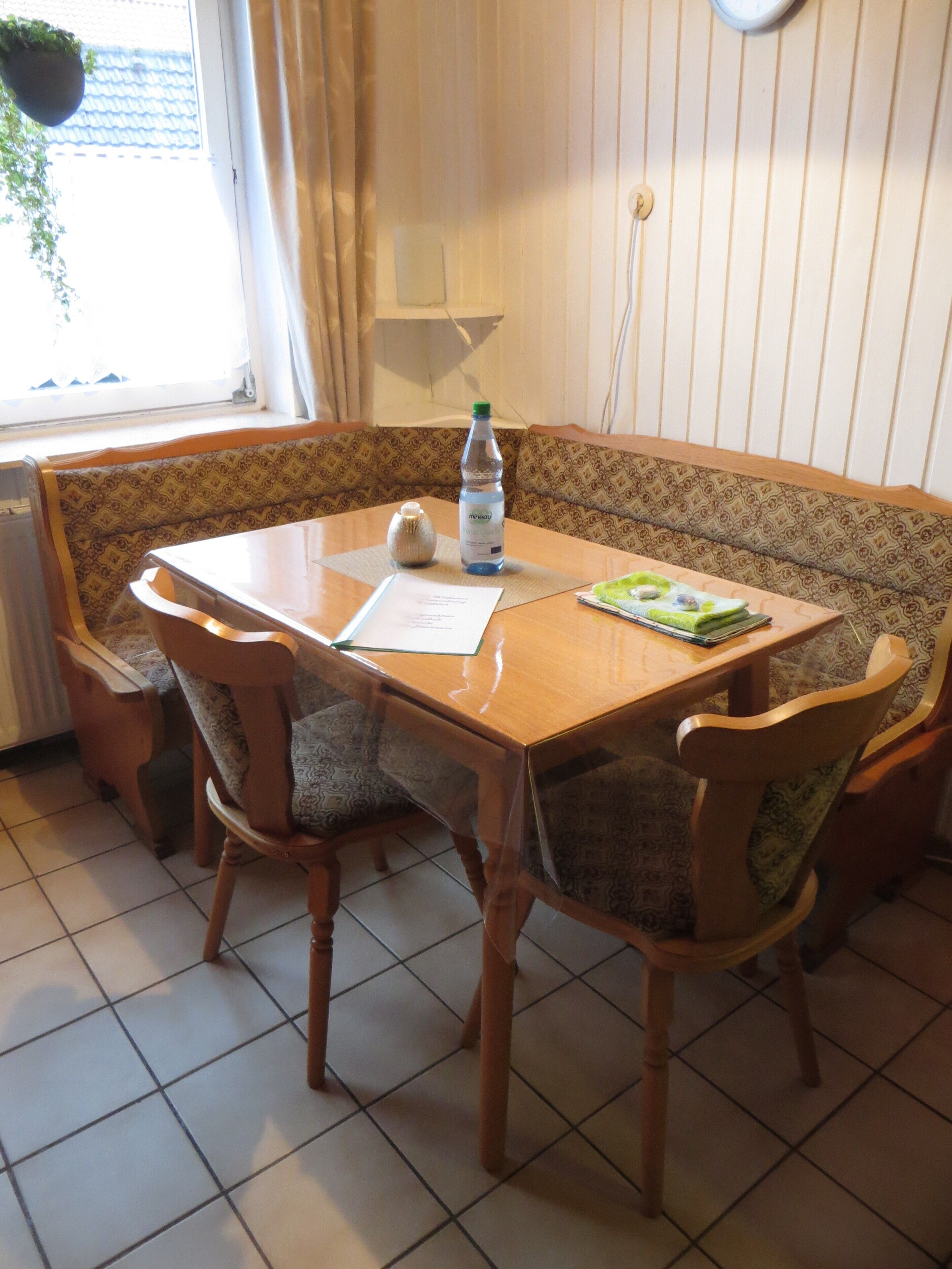 Un comedor con una mesa de madera, un banco estampado y sillas. Hay una botella y un menú sobre la mesa.