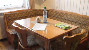 A dining area with a wooden table, patterned bench, and chairs. A bottle and menu are on the table.