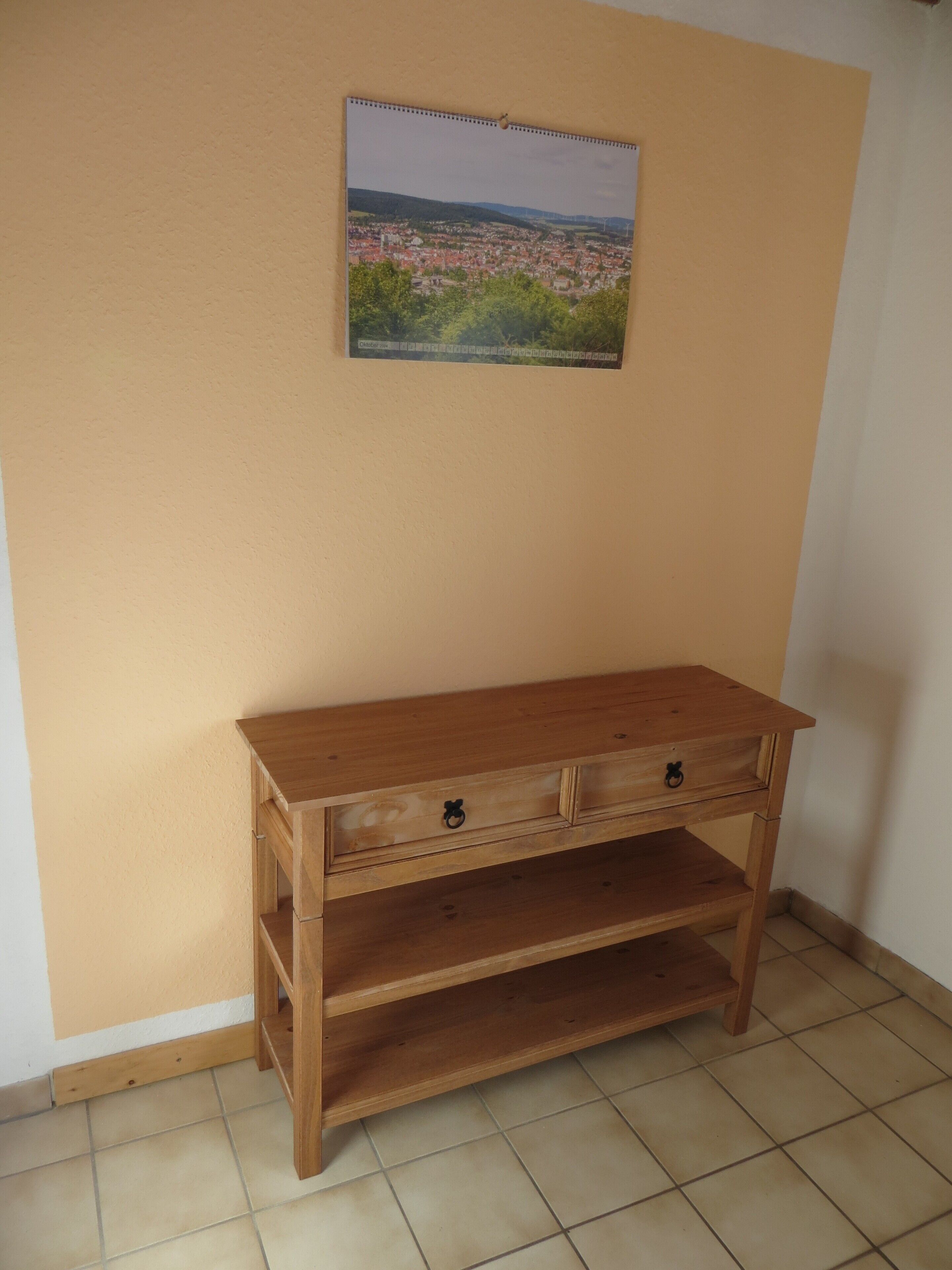 A wooden cabinet with two drawers and a shelf against a wall with a cityscape poster.