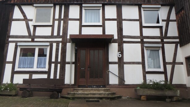 A traditional half-timbered building with a central entrance, multiple windows, and a visible number '6' on the facade.