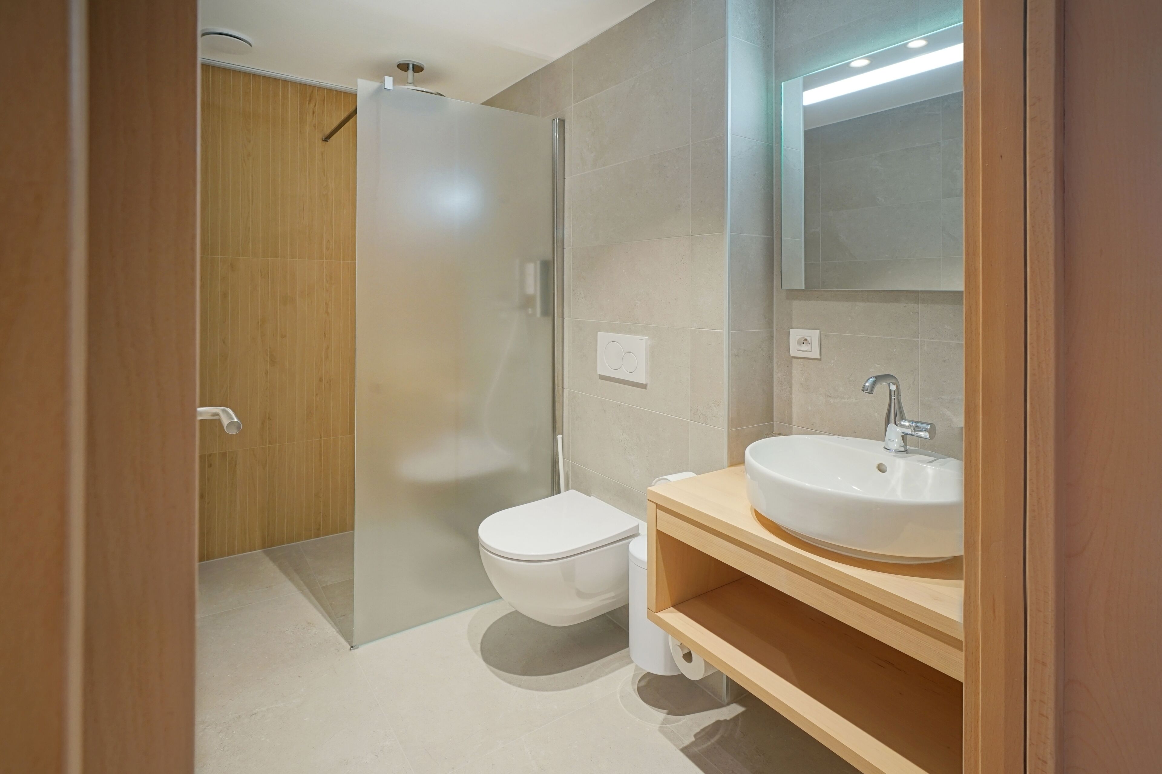Een moderne badkamer met een douchecabine van glas, een wit toilet en een houten wastafelmeubel met een wastafel.
