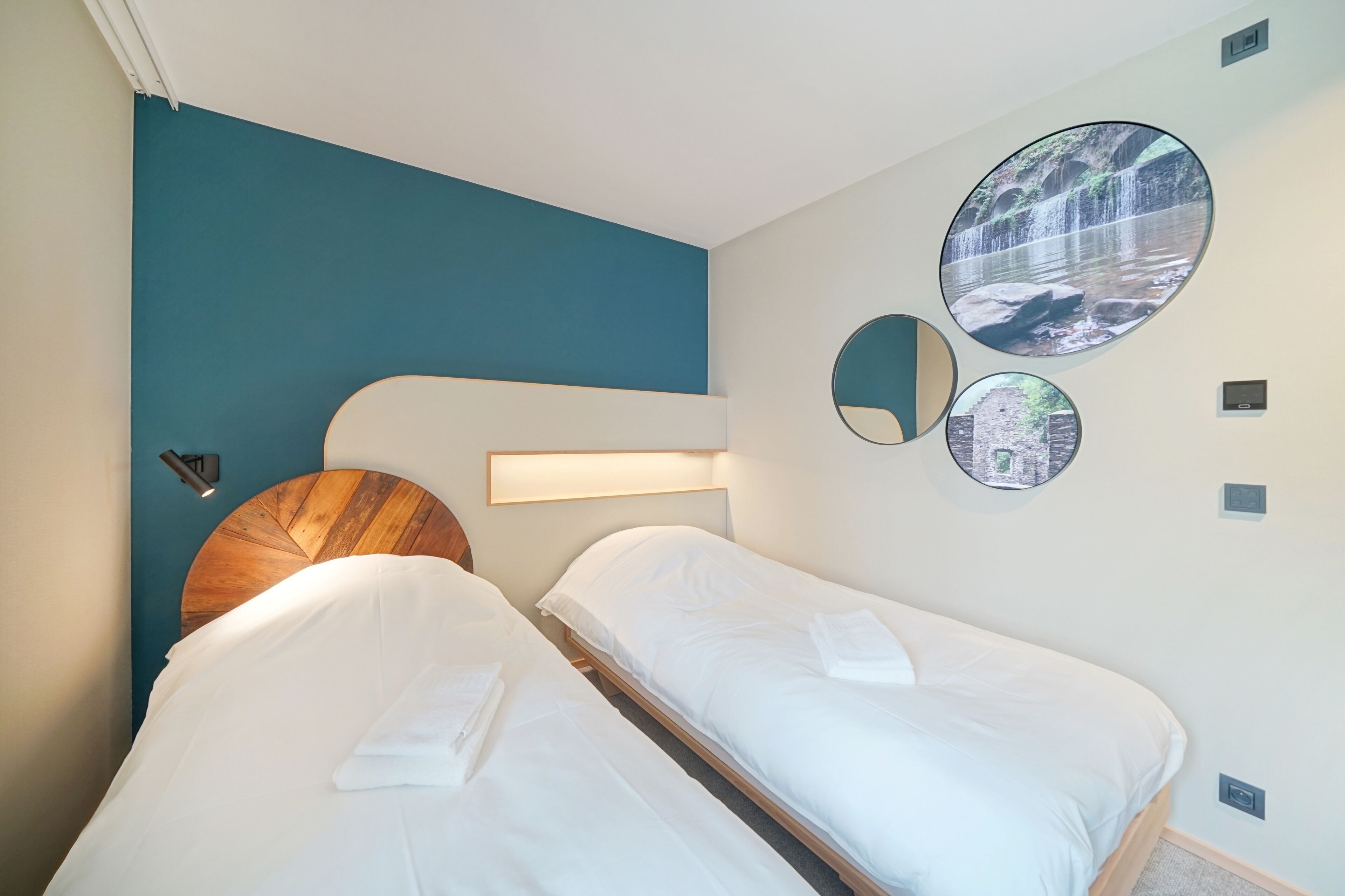 A hotel room with two beds, a wooden headboard, a teal accent wall, and circular wall art depicting nature scenes.